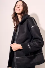Campera tipo gamulán de corte oversize, color negro, con interior y cuello de corderito sintético. Presenta cierre frontal, detalles de costuras y puños con terminación en corderito.