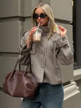 Chaqueta corta de estilo trench con estampado de cuadros pequeños, cuello alto, cierre frontal de doble botonadura y mangas con trabillas ajustables en los puños.