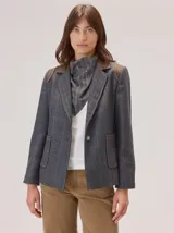 Bandana de forma triangular en tono gris oscuro con estampado de cuadros sutiles. Presenta detalles de pespuntes a mano en hilo naranja y blanco, junto con pequeños apliques decorativos que le otorgan un estilo artesanal y único.