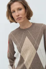 Sweater de punto con diseño de rombos en tonos tostado, beige y blanco, con detalles en color terracota en las mangas. Presenta cuello redondo y puños acanalados.