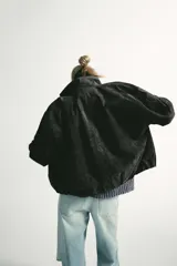 Cazadora de ante con cuello subido, manga larga con puños y bajo elástico. Presenta cierre frontal con cremallera metálica y botones a presión ocultos por solapa, además de bolsillos delanteros.