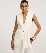 Chaleco sastre alargado color blanco hueso con finas rayas verticales. Presenta cuello tipo blazer, cierre cruzado con un botón metalizado y un lazo ancho para ajustar a la cintura.