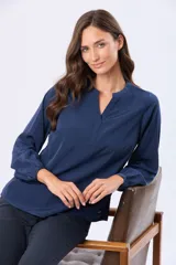 Blusa de manga larga en color azul marino, con escote en V y diseño de doble capa en el frente. Presenta puños elásticos y un pequeño aplique metálico decorativo en el ruedo.