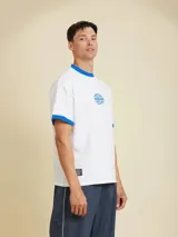 Remera blanca de manga corta estilo ringer, con cuello redondo y ribetes en color azul. Presenta un pequeño estampado circular en el pecho.