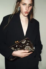 Bolso tipo clutch de efecto terciopelo color marrón, con bordados florales, apliques de brillos y lentejuelas. Cuenta con cierre de clip metálico dorado y cadena metálica extraíble.