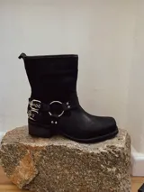 Bota corta de cuero color marrón, con taco cuadrado y punta redondeada. Presenta una correa con hebillas y argolla metálica decorativa alrededor del tobillo. Cuenta con cierre lateral.