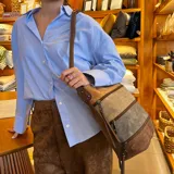 Bandolera de diseño tricolor con paneles en tonos marrón, beige y gris. Presenta múltiples cierres frontales, correa larga regulable y compartimento principal con cierre superior.