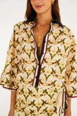 Camisa de algodón con estampado floral y de aves, cuello camisero oscuro y cierre frontal parcial con botones. Mangas amplias de largo codo con ribetes en contraste.