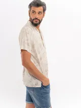 Camisa de manga corta color beige con estampado tropical de hojas, cuello camisero abierto y cierre frontal de botones.