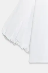 Camisa de algodón con cuello solapa y cierre frontal con botones ocultos. Presenta mangas abullonadas por debajo del codo con terminación elástica.