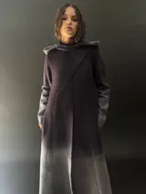 Tapado largo de lana merino color gris oscuro con teñido degradado en gris claro en ruedo, mangas y capucha. Tiene corte recto, bolsillos laterales y cierre cruzado con broches a presión ocultos en los hombros.