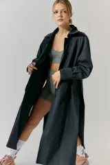 Trench midi negro confeccionado en algodón y nylon repelente al agua, con cuello clásico, cierre cruzado con botones, cinturón ajustable, mangas largas con puños abotonados, bolsillos internos altos y tajos laterales.