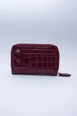 Billetera chica de cuero negro con textura tipo cocodrilo, cierre exterior, bolsillo para monedas con cierre en la parte trasera, múltiples ranuras para tarjetas y billetes, y forro rojo.