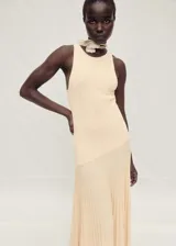 Vestido largo de punto fino color beige, con diseño evasé y plisado en la parte inferior. Presenta cuello halter y diseño sin mangas.