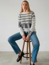 Buzo de tejido con textura suave, de corte holgado y manga larga. Presenta un diseño de rayas horizontales en tonos blanco, gris y negro, con un patrón gráfico en la parte inferior.