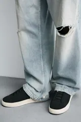 Zapatilla de piel color negro con acabado serraje, cordonera oculta y suela plana a contraste en color crema.