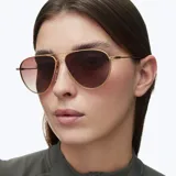 Lentes de sol estilo aviador con montura metálica fina en color dorado y lentes degradadas en tono marrón. Presentan un diseño ligero con puente doble y terminales de patillas en acetato.
