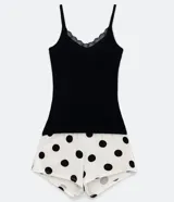 Conjunto de pijama short doll, con top de canalé negro con encaje en el escote y pantalón corto blanco con estampado de lunares negros y cintura elástica.