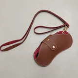 Estuche para lentes de diseño ergonómico y minimalista, confeccionado en cuero sintético con textura granulada. Cuenta con cierre magnético frontal, costuras a la vista en color contrastante y una correa de mano extraíble.