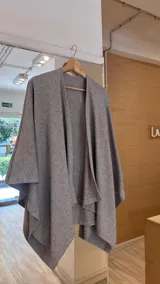 Ruana de tejido de punto fino en color beige, con diseño abierto y caída fluida.