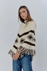 Poncho tejido de lana en color crudo con detalles geométricos en marrón oscuro y flecos en el ruedo.