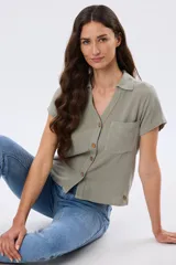 Camisa de lino color verde militar, de manga corta, con cuello camisero, cierre frontal con botones y un bolsillo aplicado en el pecho.