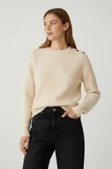 Sweater de tejido de punto color crema, con cuello redondo a la base y tres botones decorativos en el hombro izquierdo.