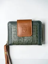 Mini billetera de cuero con diseño bicolor en verde aceituna y marrón. Presenta una textura tipo reptil en el cuerpo principal y una solapa frontal con el logo de un búho grabado. Incluye una correa de muñeca desmontable en color marrón.