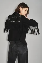 Camisa negra de gamuza caprina con cuello y hombros adornados con tachas metálicas plateadas. Presenta flecos decorativos en el canesú y botones plateados en el frente.