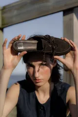Zapatos tipo mocasín destalonados de gamuza marrón, estilo náutico con cordones frontales y ojales metálicos.