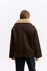Campera de estilo aviador en color marrón oscuro, con exterior efecto gamuza e interior de corderito sintético color beige. Presenta cuello amplio, cierre frontal con botones y bolsillos laterales.