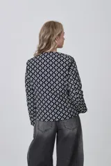 Chaqueta de manga larga con cuello a la base y cierre frontal. Presenta un estampado geométrico repetitivo en blanco y negro.