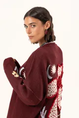 Saco de punto color vino con diseño holgado, cuello redondo y mangas largas. Presenta un gran bordado central en la espalda con forma de flor en tonos crema y rojo, acompañado de un pequeño bordado de sol y una frase bordada en la parte inferior.