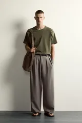 Pantalón relaxed fit de color blanco off-white, confeccionado en tejido con lino. Cuenta con pliegues frontales en la cintura, bolsillos delanteros y cierre frontal con cremallera y botón.