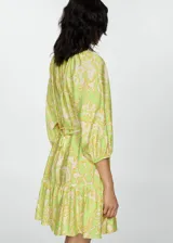 Vestido corto de tejido fluido con estampado paisley en tonos verde lima y crema. Presenta escote en pico, cierre frontal con botones, mangas tres cuartos con puños elásticos y falda con detalle de volante en el bajo. Incluye un cinturón fino del mismo tejido para ajustar a la cintura.