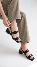 Sandalias de cuero charol negro con taco cuadrado de 4 cm, tiras frontales y tira ajustable con hebilla metálica en el talón.