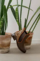 Botinetas de cuero color marrón con diseño tipo chelsea, con paneles laterales elásticos y detalle de cuero texturizado con acabado metalizado en el talón. Poseen taco bajo cuadrado y terminación redondeada.