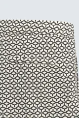 Bañador corto de hombre con cintura elástica ajustable mediante cordón blanco. Presenta un estampado geométrico repetitivo en tonos oscuros (negro/marrón oscuro) y blanco/beige. Incluye bolsillos laterales y un bolsillo trasero de vivo.