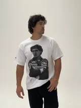 Remera blanca de algodón con estampa fotográfica frontal de Ayrton Senna con su traje de piloto de Fórmula 1. Presenta un corte holgado y cuello redondo.