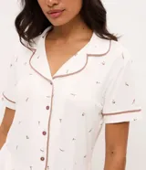 Pijama corto de dos piezas confeccionado en viscolycra blanca con estampado floral y vivo en contraste. Incluye una camisa de manga corta con cuello solapa y cierre frontal de botones, y un short con cintura elástica.