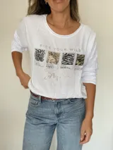 Remera blanca de manga larga, con cuello redondo y corte semi holgado. Presenta un estampado frontal con la frase "PICK YOUR WILD" en dorado y cuatro recuadros con diferentes "animal prints" (pitón, leopardo, cebra y tigre), con detalles en dorado y pedrería.