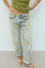 Jeans de tiro bajo y corte holgado, color celeste con estampado floral en tonos amarillos y verdes. Presenta diseño de cinco bolsillos, trabillas para cinturón y dobladillo con vuelta en los bajos. Cierre frontal con cremallera y botón metálico.