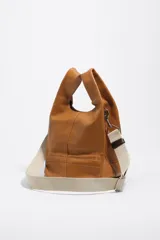 Bolso de mano Bimba y Lola modelo Paper mediano, confeccionado en cuero color tostado con estructura blanda, asas superiores y correa de hombro ajustable en color beige. Presenta costuras visibles, logo metálico de la marca en la parte inferior y cierre principal.