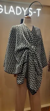 Ruana en paño blanco y negro con diseño geométrico, con presilla para sujetar y vivo negro en todo el borde.