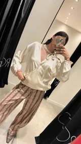 Blusa de satén color beige, con diseño reversible que permite usar el escote pronunciado hacia el frente o hacia la espalda. Presenta mangas largas abullonadas con puños elásticos y un lazo integrado en el cuello para anudar.