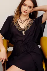 Vestido negro de viscosa con escote en V profundo y detalles bordados en dorado en el cuello. Cuenta con mangas cortas amplias y cordón ajustable en la cintura.