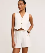 Short sastre de cintura alta, color blanco, con bolsillos laterales y detalles de tachuelas metalizadas.