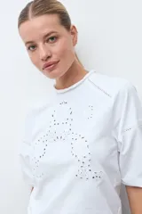Remera blanca de manga tres cuartos, con cuello redondo y detalles de bordado calado en la parte frontal y hombros.
