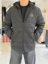 Campera puffer impermeable color negro, con capucha desmontable y cierre frontal. Cuenta con bolsillos laterales con cierre y parche redondo en el pecho con la inscripción 'TURK'.