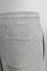 Pantalón jogger gris de corte regular fit, confeccionado en tejido de algodón con interior afelpado. Cuenta con cintura elástica ajustable con cordón, bolsillos laterales de vivo y traseros de plastrón. Presenta un texto estampado en color bordó en la pernera y bajo acabado en puño con elástico. Incluye un parche con logo combinado a contraste en la cintura.